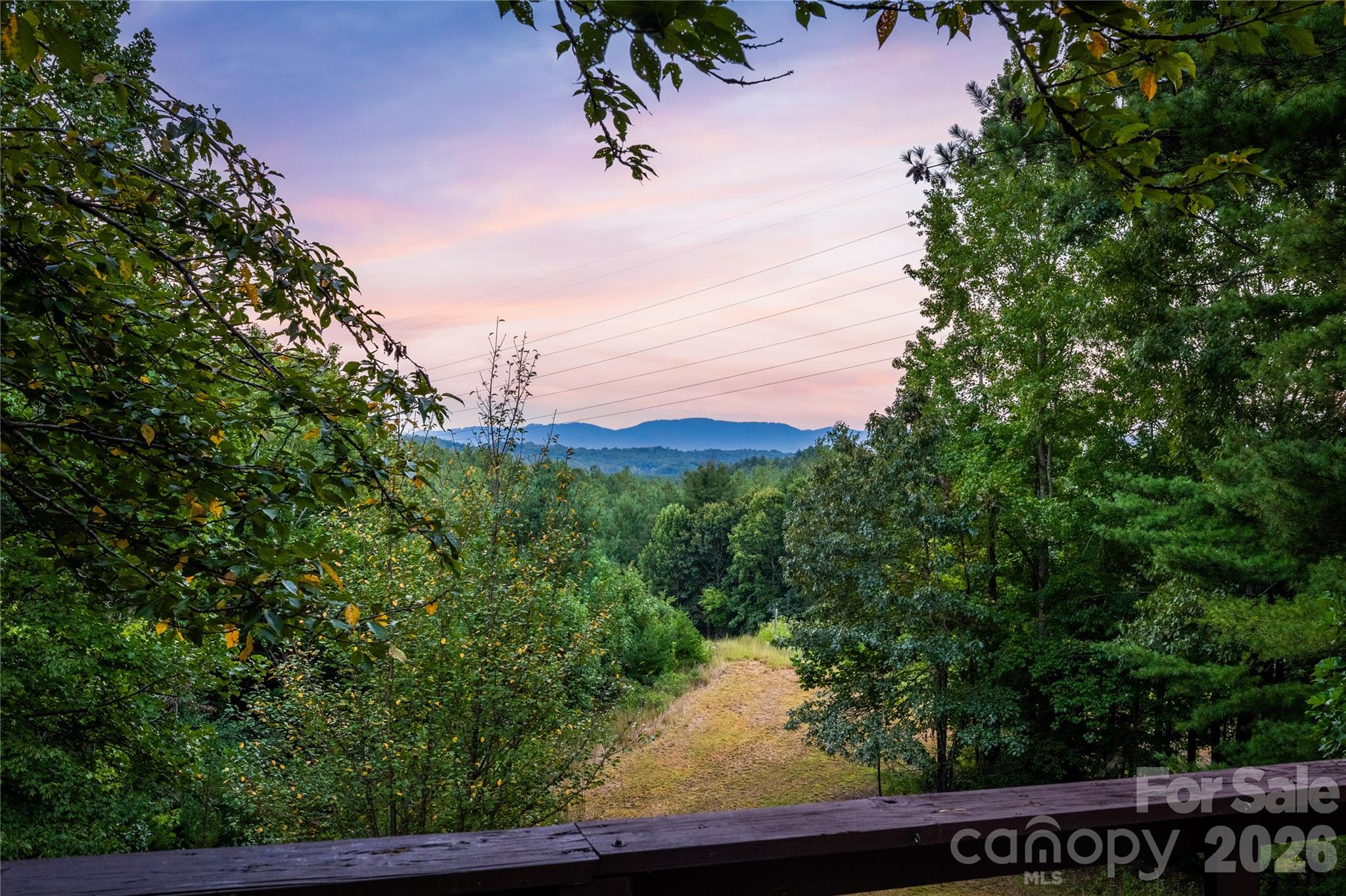 Wooded property with a grassy clearing, distant mountain ridge, and pink dusk sky.