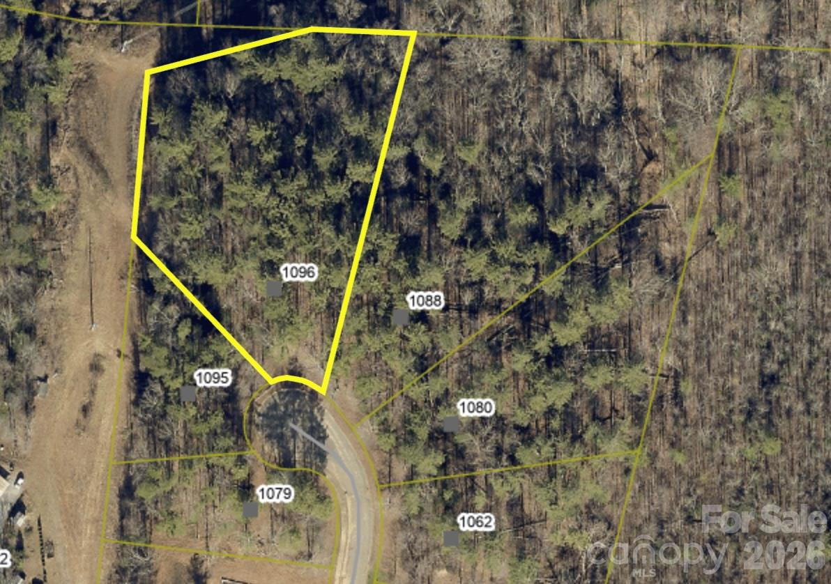 Aerial view of wooded lot 1096 outlined in yellow beside a curved road.