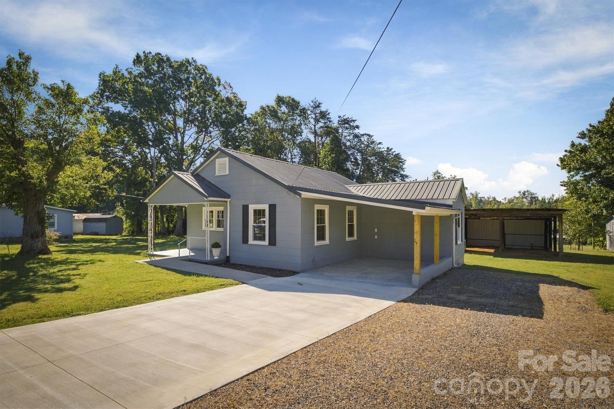 Gray single-story home with a metal roof, covered porch, driveway, and detached carport.