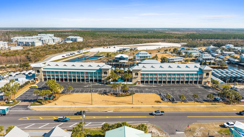 Aerial view of a coastal shopping center with two retail buildings, parking, and surrounding development.