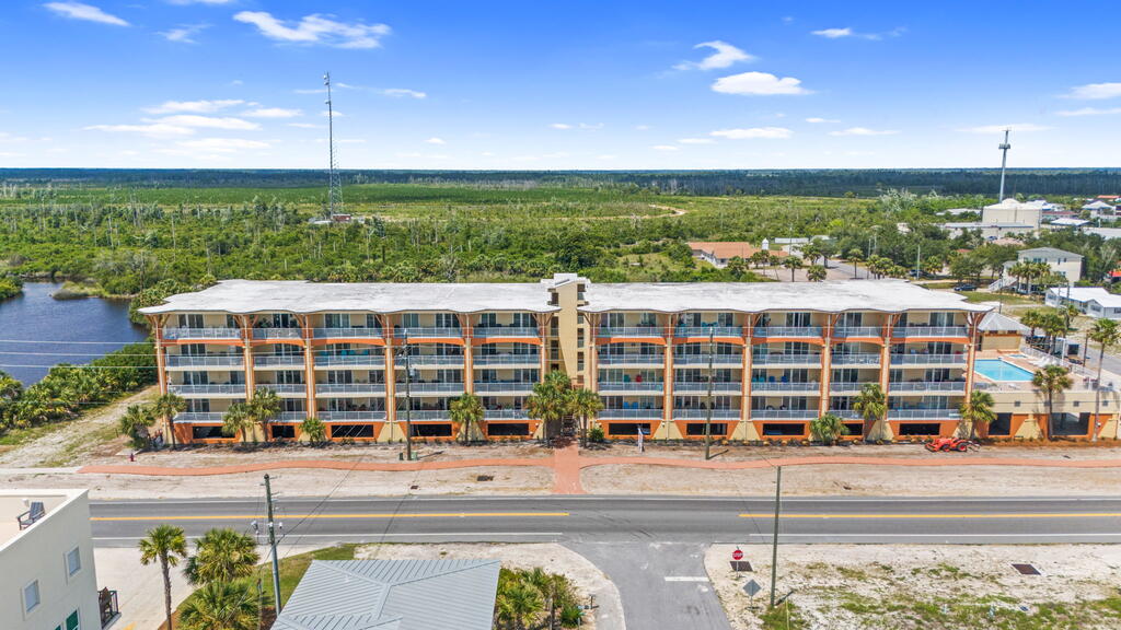 Multi-story condominium with rows of balconies and a pool, viewed from across the road.