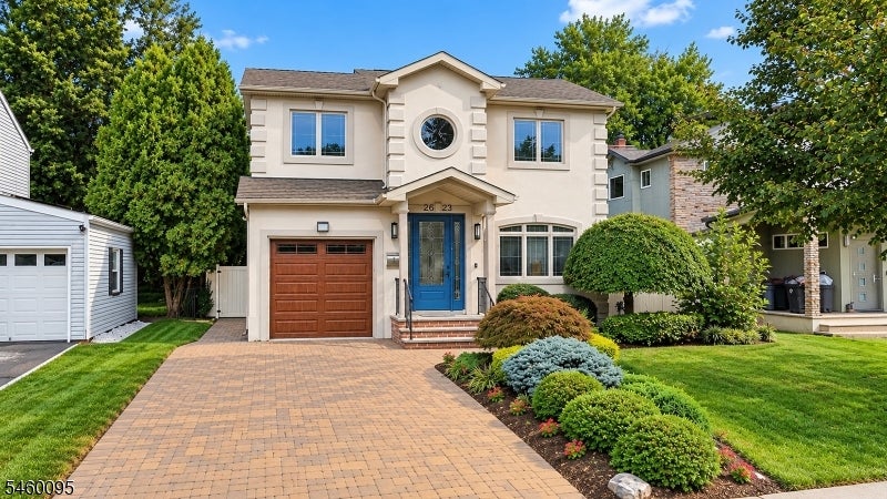 Two-story cream home with a blue front door, brown garage, paver driveway, and landscaped garden beds.