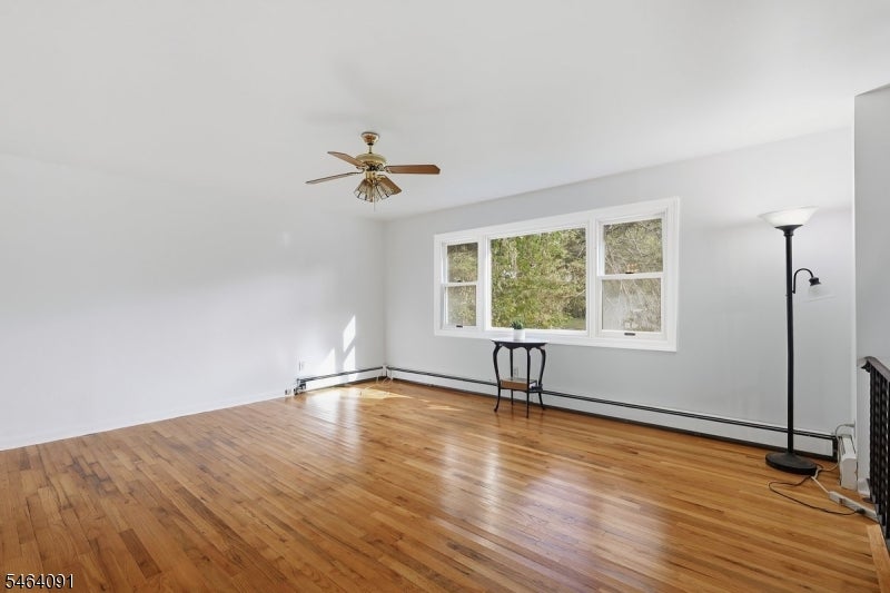 Mostly empty living room with polished hardwood floors and a wide window overlooking trees.