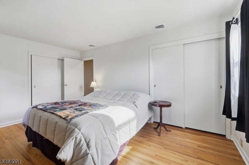 Bedroom with a large white-quilted bed, hardwood floors, and sliding-door closets.
