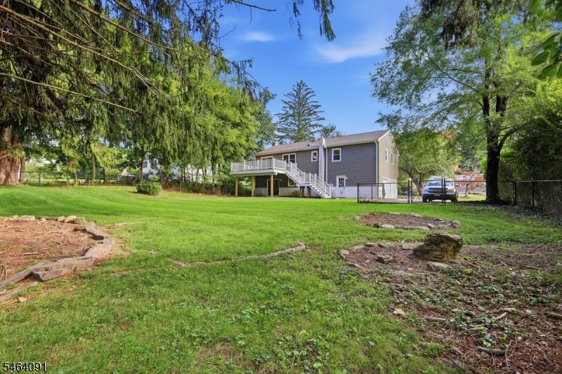 Gray two-story house with an elevated deck and stairs beyond a broad, tree-lined lawn.