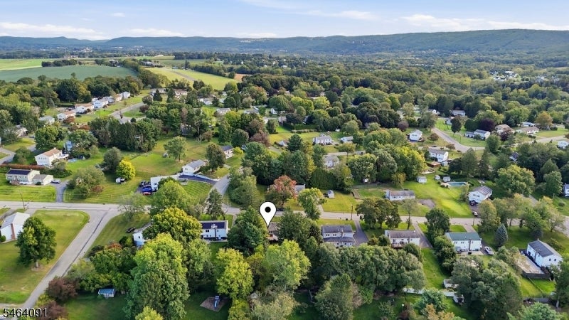 Aerial view of a leafy neighborhood, with a map pin among homes and wooded hills beyond.