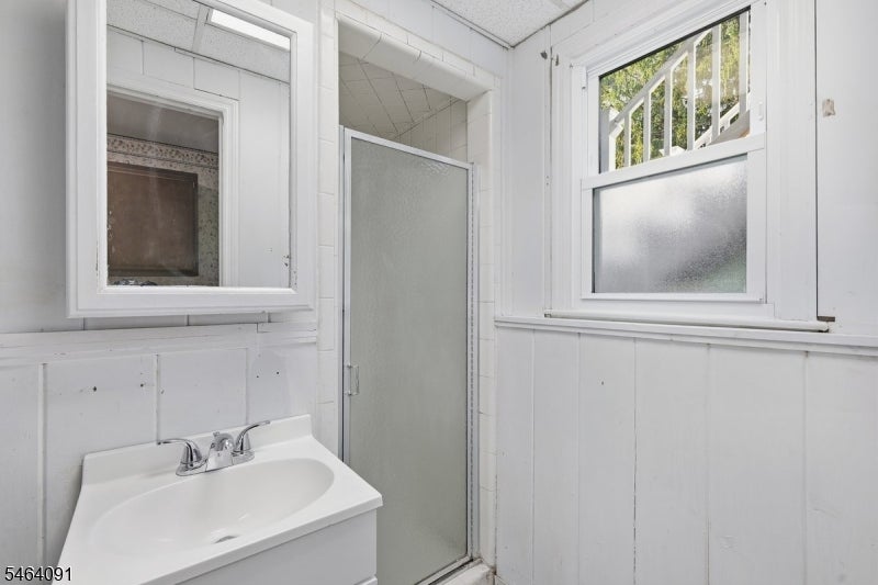 Bathroom with a white sink vanity, frosted-glass shower door, and two windows.