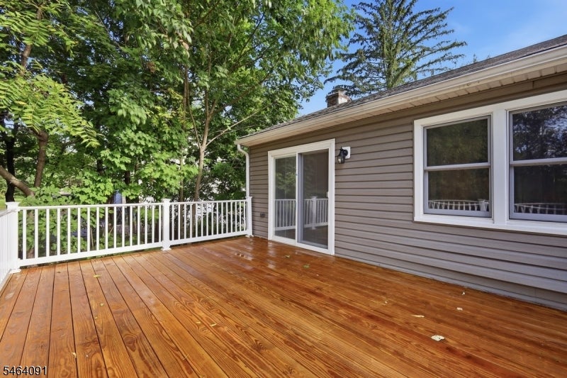 Wooden deck beside a gray-sided home, with white railing and leafy trees.