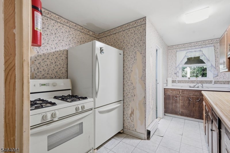 Kitchen with floral wallpaper, white appliances, dark wood cabinets, and a window above the sink.