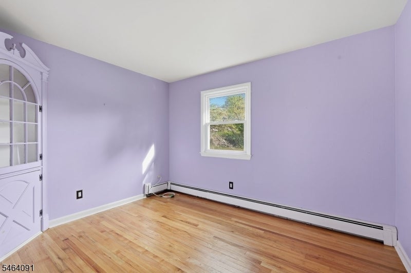 Vacant room with lavender walls, hardwood floors, and a white-trimmed window.