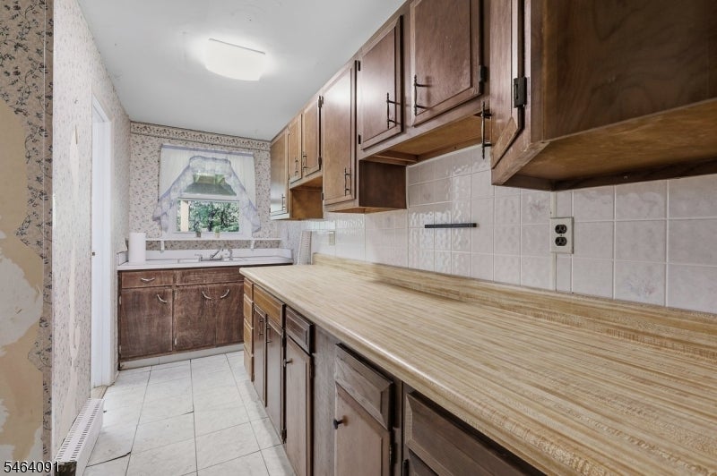 Kitchen with dark wood cabinets, a long countertop, and a window above the sink.