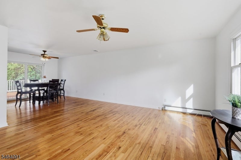 Open room with hardwood floors, a dining table by sliding glass doors, and two ceiling fans.