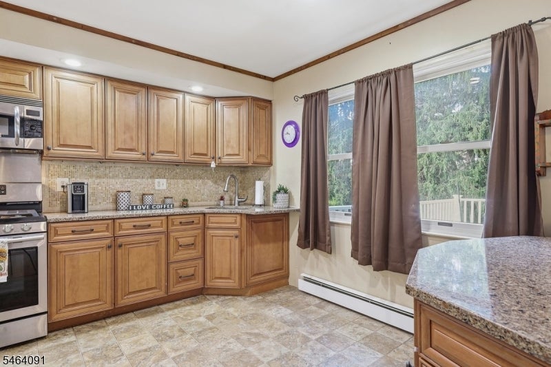 Kitchen with wood cabinets, granite counters, stainless steel appliances, and large windows overlooking a deck.