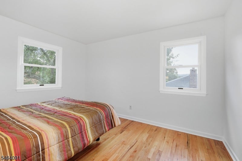 Bedroom with a multicolored striped bedspread, two windows, and light wood floors.