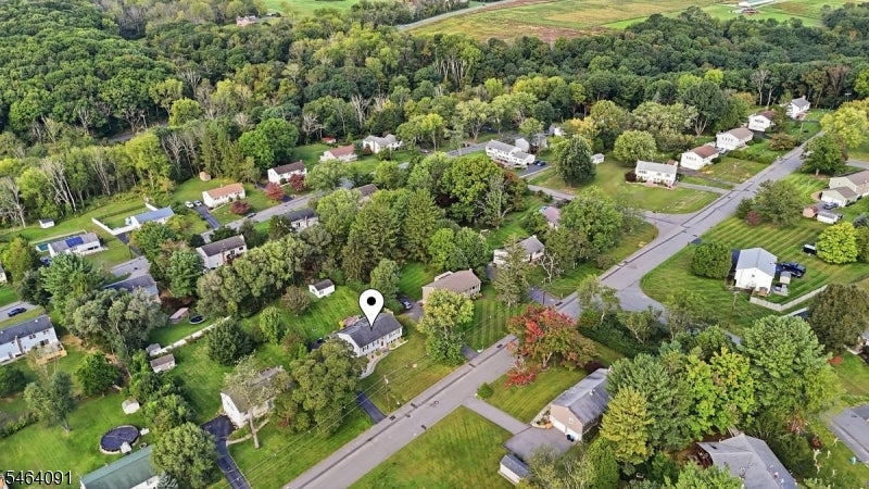 Aerial view of a detached home beside a road in a tree-lined residential neighborhood.