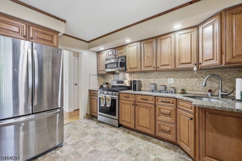 Kitchen with warm wood cabinets, granite counters, stainless-steel appliances, and a tiled backsplash.
