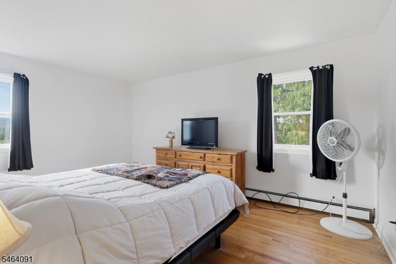 Bedroom with a large bed, wooden dresser and television, black curtains, and hardwood floors.