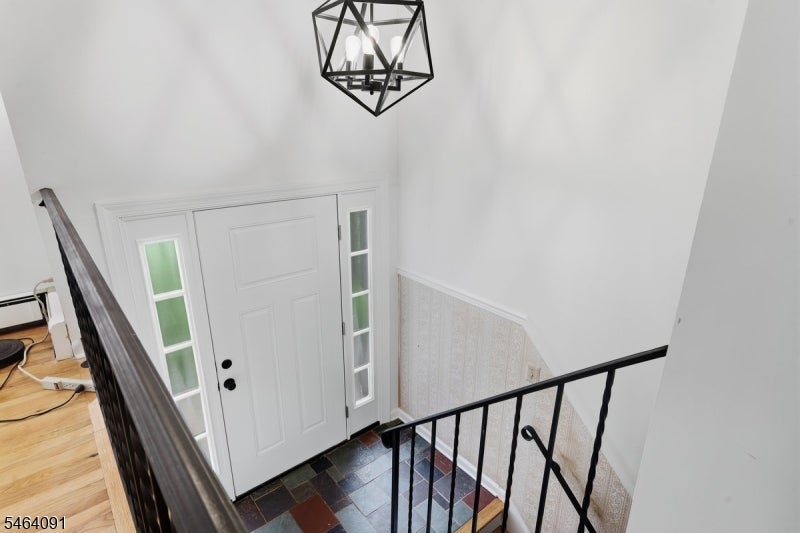 Entry foyer with a white front door, dark tiled floor, black railings, and geometric pendant light.