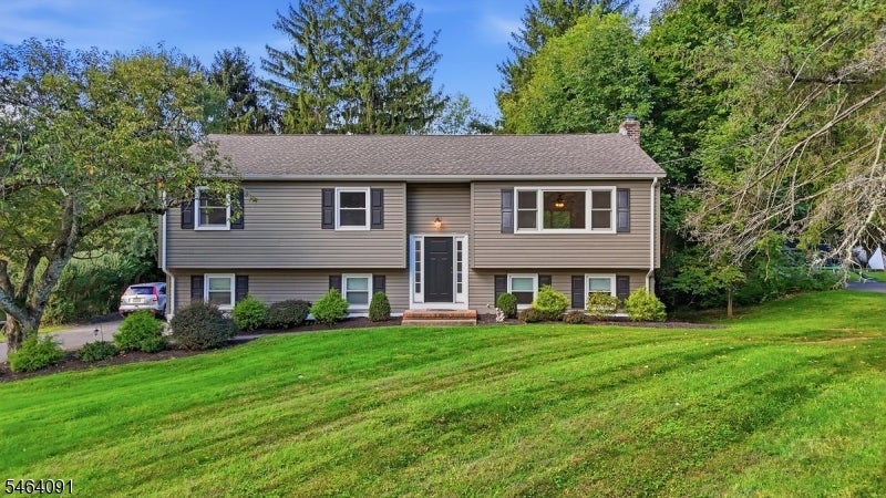 Two-story split-level home with taupe siding, a dark central entrance, and a broad green lawn.