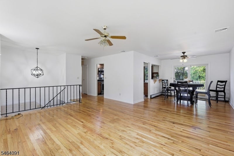 Open living and dining area with hardwood floors, black stair railing, and a dining table by large windows.