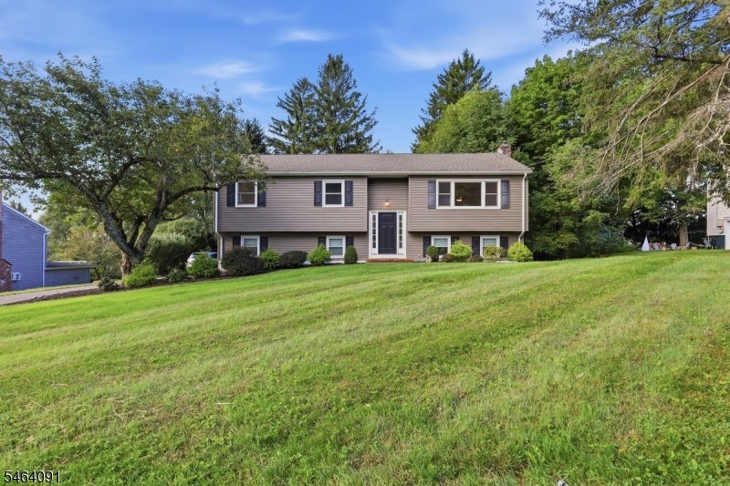 Raised ranch home with gray siding and dark shutters above a broad sloping lawn.