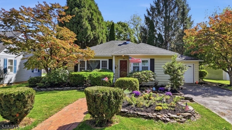 Single-story ranch-style house with a brick walkway, landscaped garden, and mature autumn trees.