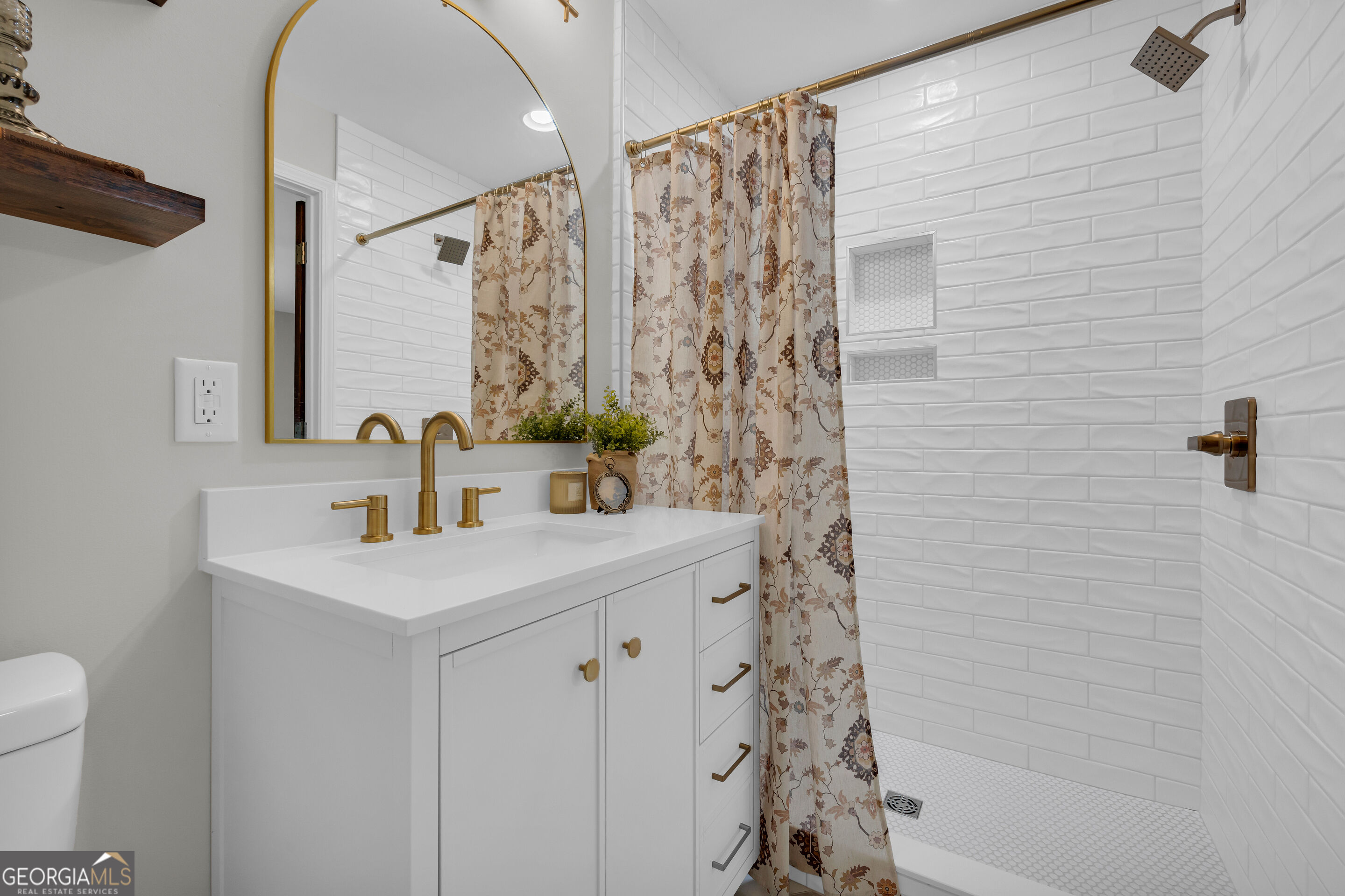 Bathroom with a white vanity, gold fixtures, and a white subway-tile shower.