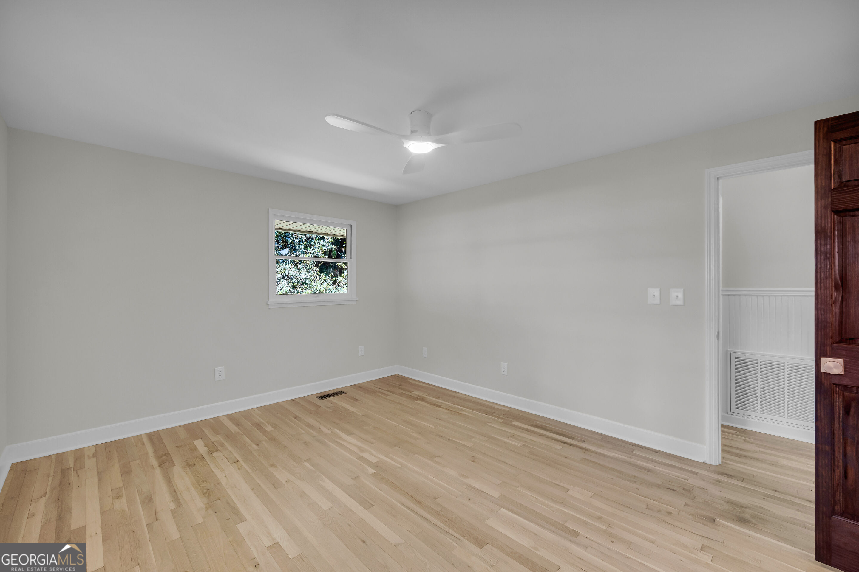 Empty room with light hardwood floors, ceiling fan, small window, and doorway to an adjoining room.