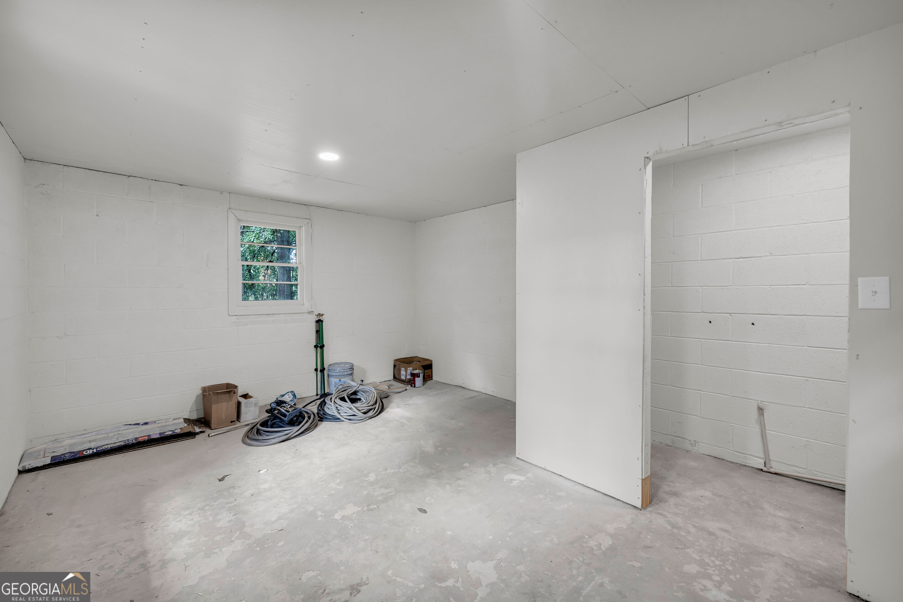 Utility room with white block walls, a small window, and coiled hoses on the concrete floor.