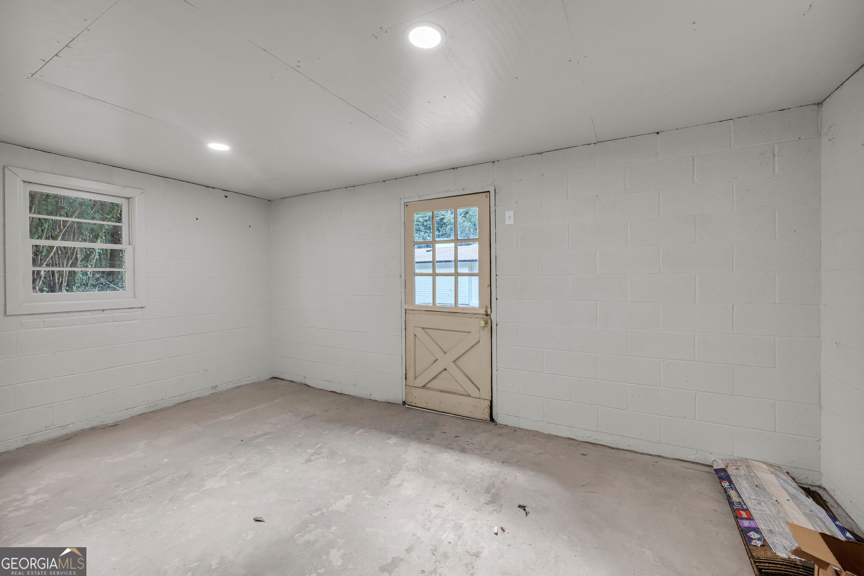 Unfinished white block room with a concrete floor, window, and glass-paneled exterior door.