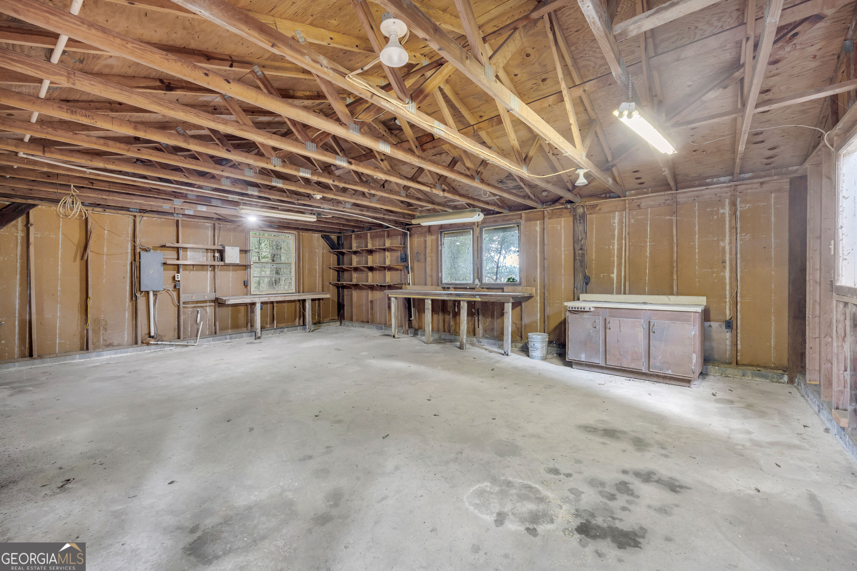 Unfinished garage with exposed wood rafters, concrete floor, workbenches, and shelving.