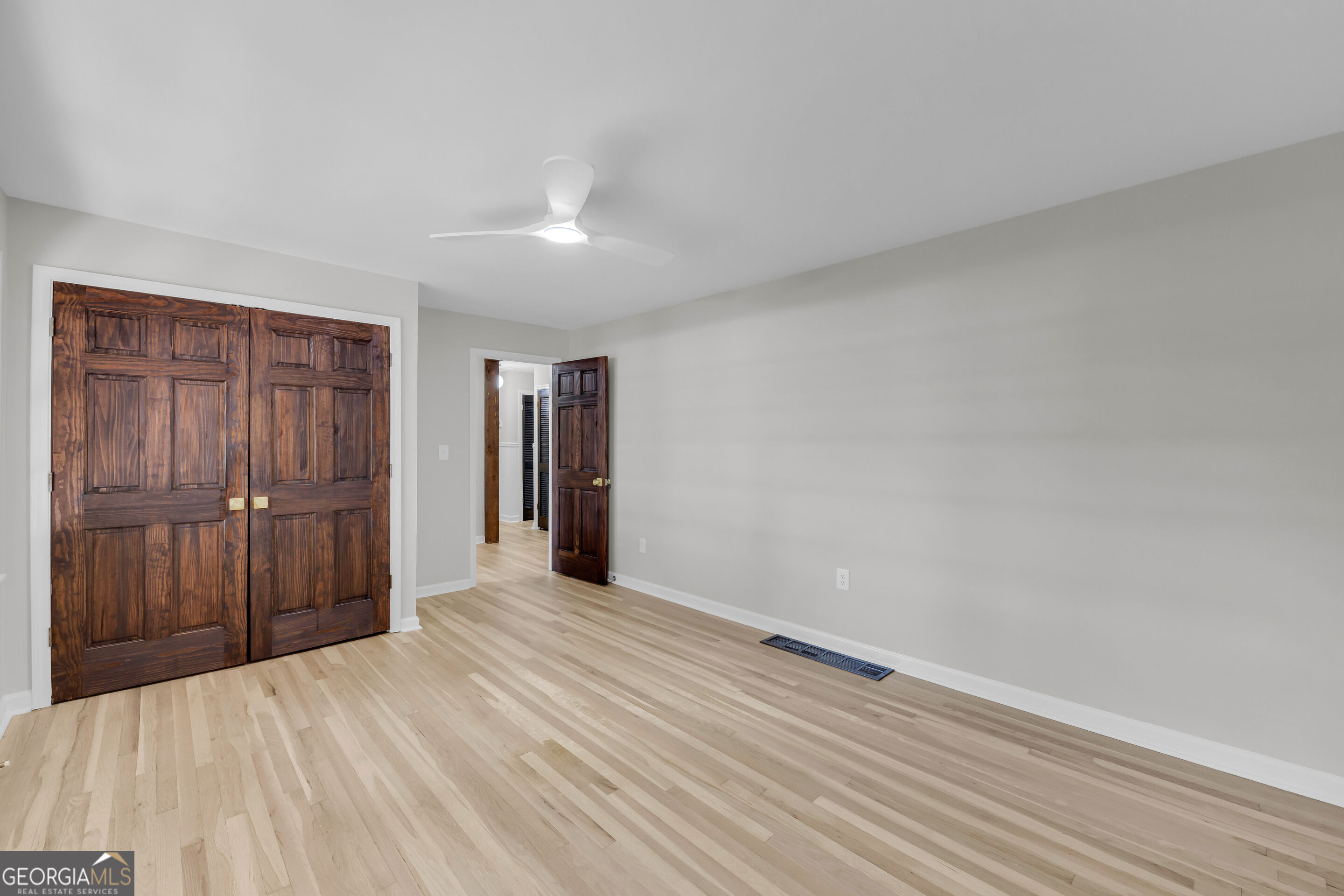 Empty room with light wood flooring and dark wooden double closet doors.