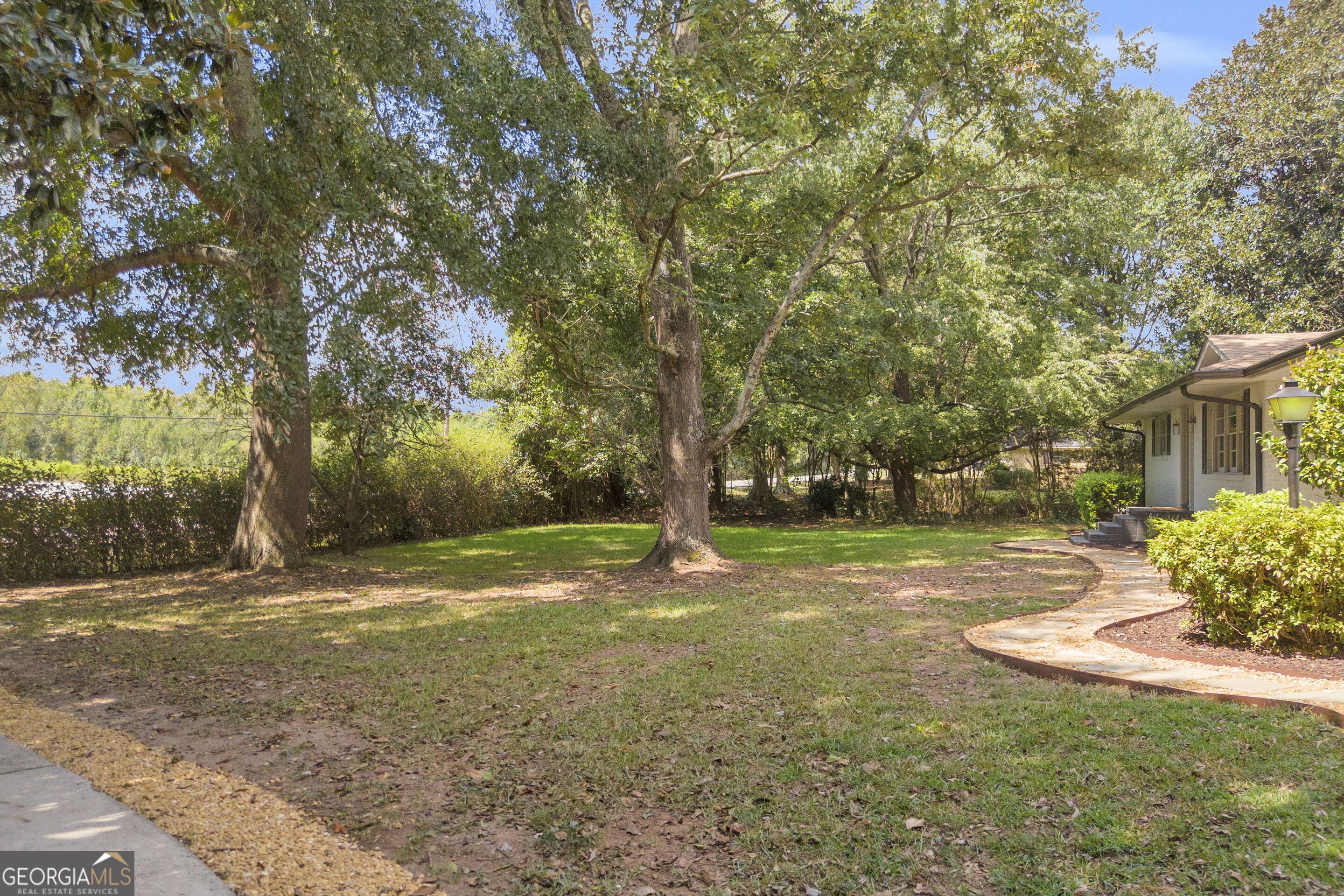 Shady front yard with mature trees, a broad lawn, and a curved walkway to the house.