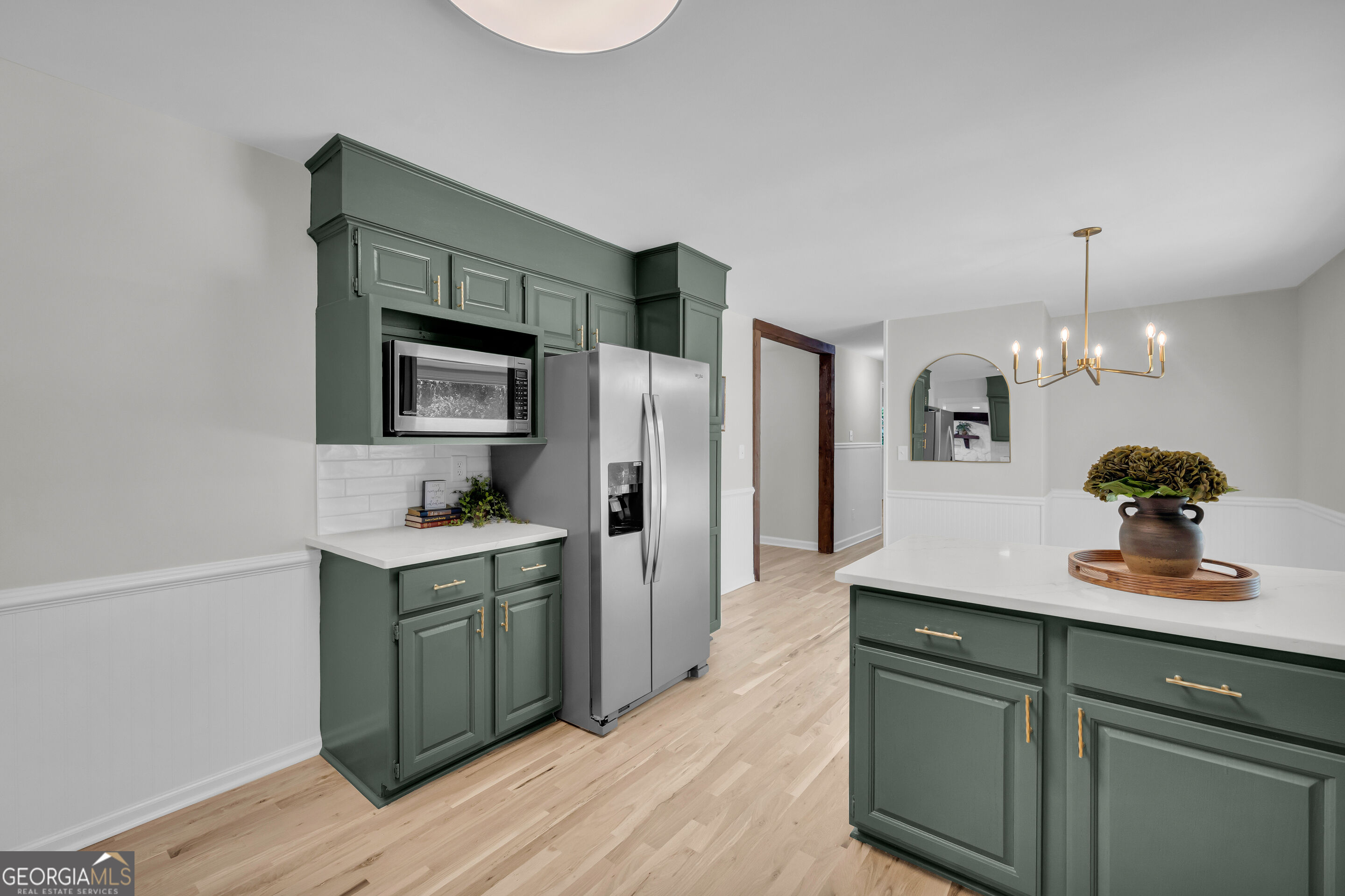 Kitchen with deep green cabinetry, stainless steel appliances, and a large white island.