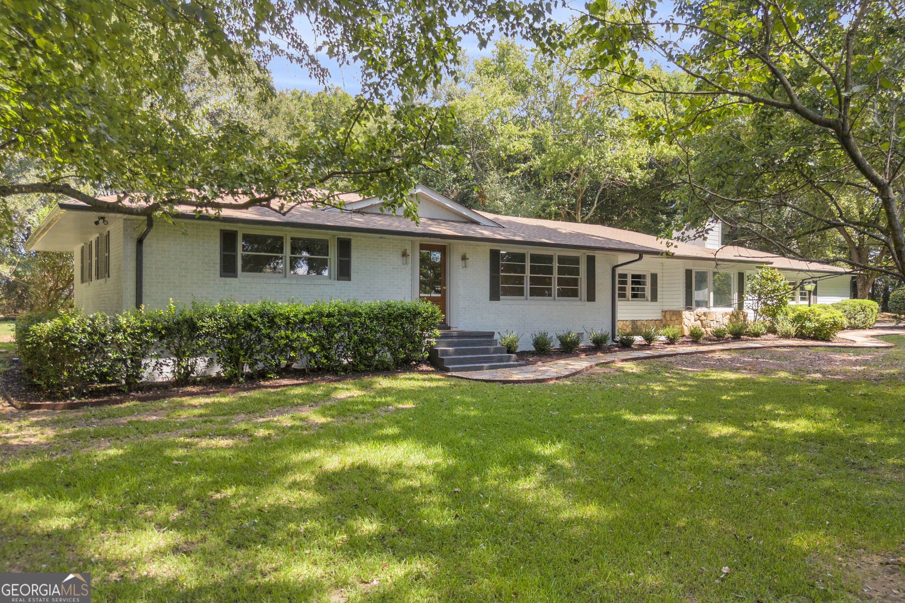 Single-story brick ranch with front steps and a broad lawn shaded by mature trees.
