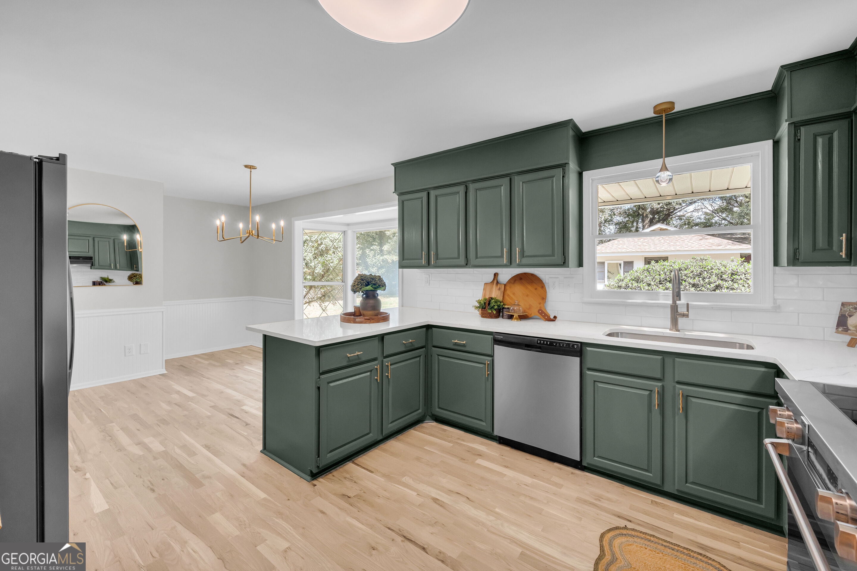 Kitchen with dark green cabinets, white counters, stainless steel appliances, and light wood floors.