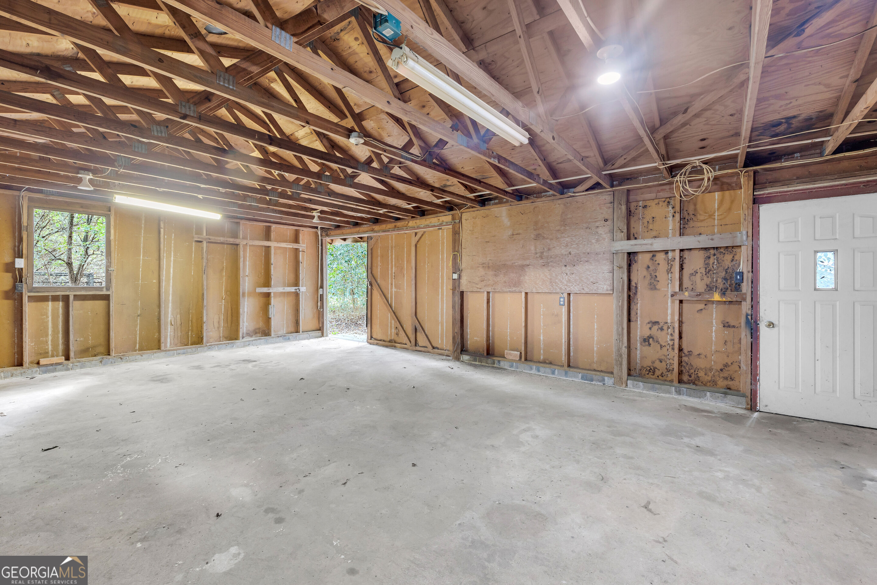 Unfinished, empty garage with exposed roof trusses, concrete floor, and exterior doors.