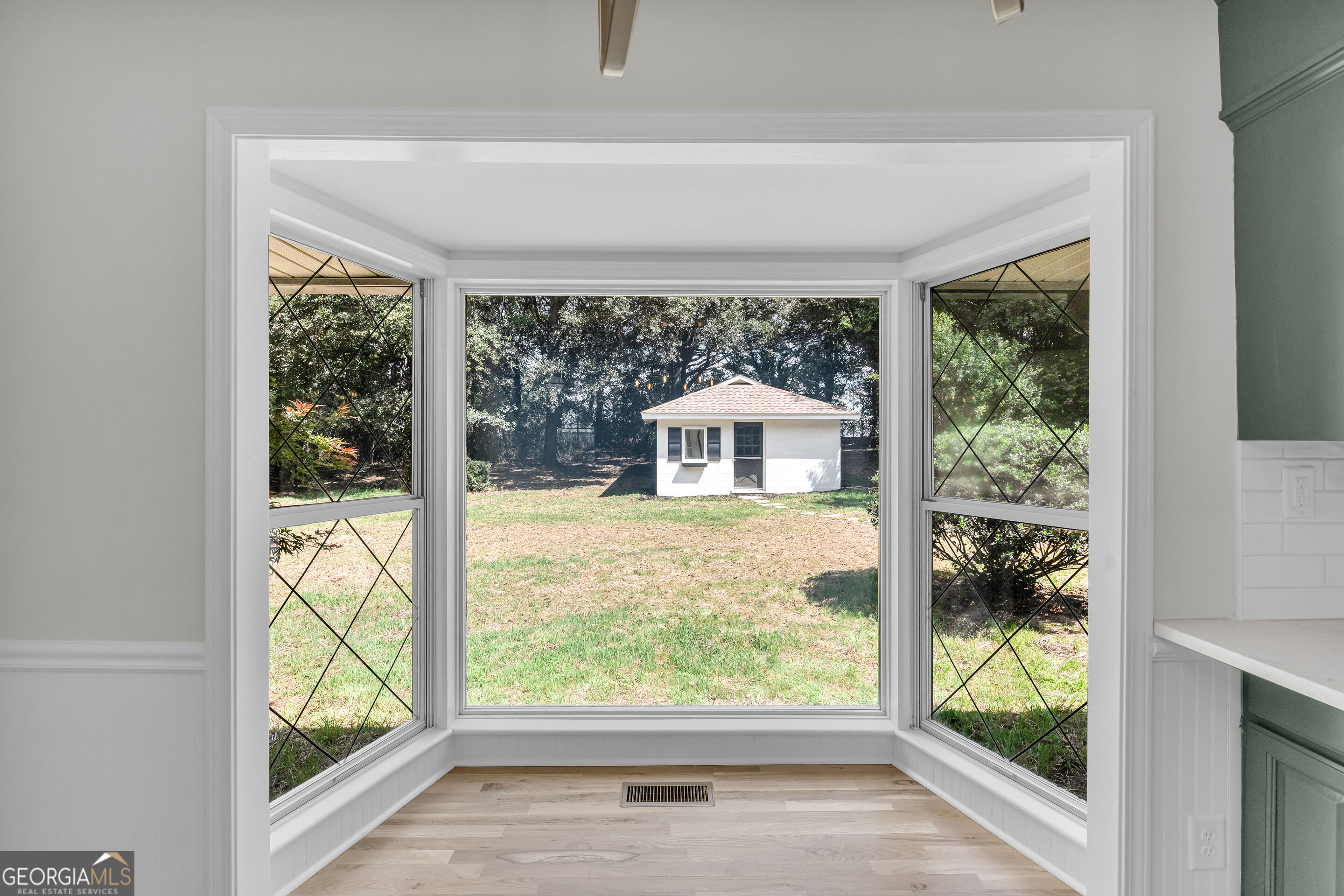 Sunroom with expansive bay windows overlooking a grassy yard and small detached outbuilding.