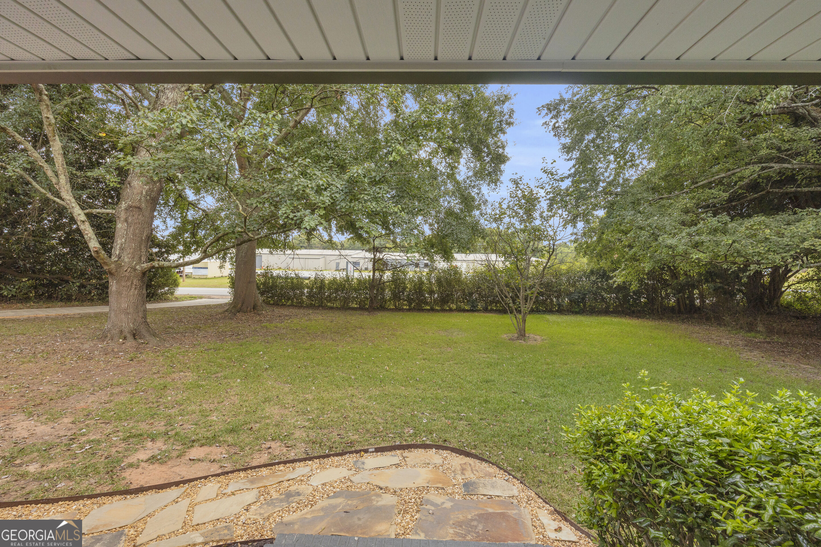 Covered patio overlooking a grassy backyard with mature trees and a stone patio.