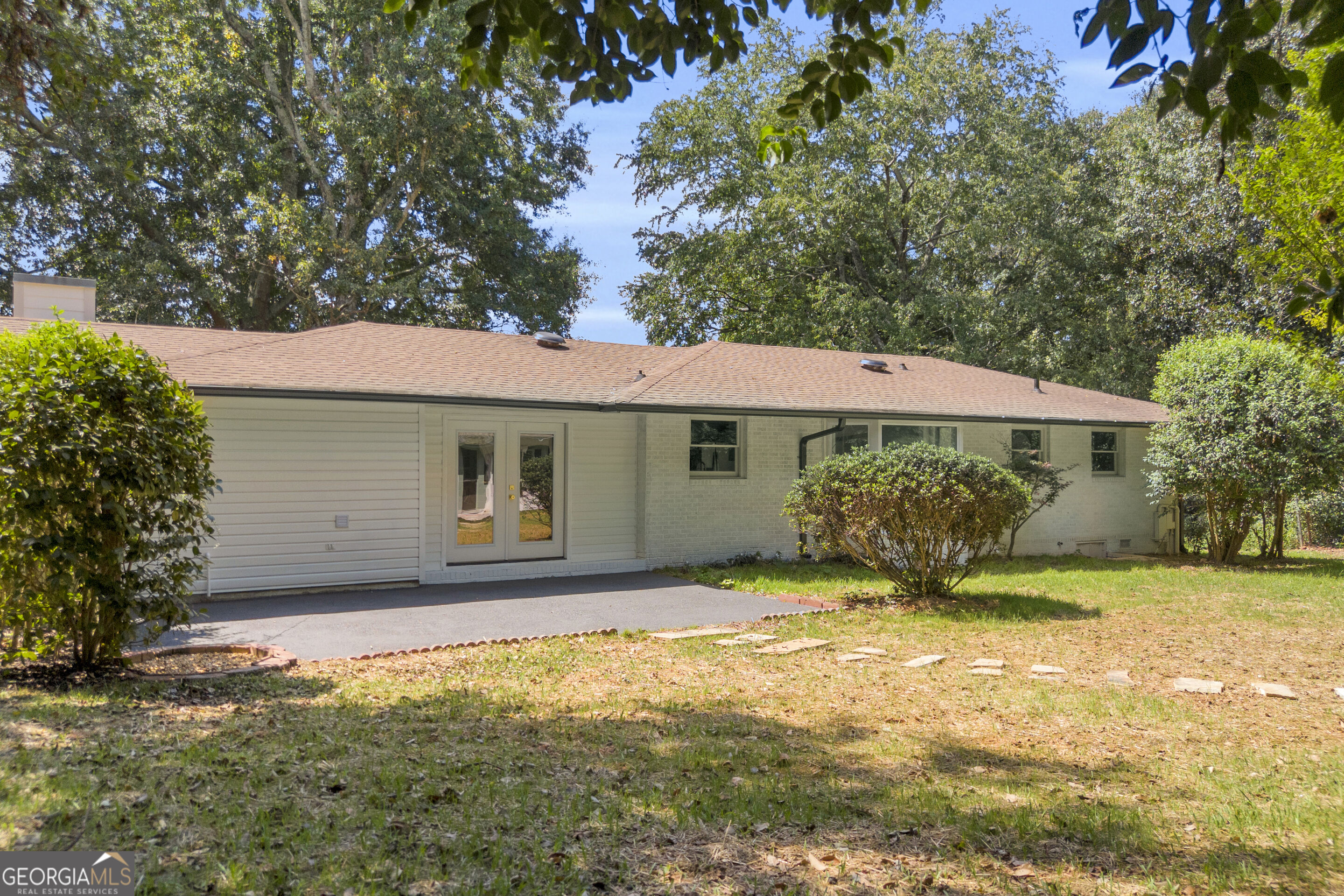 Single-story home with French doors, a paved patio, and a leafy, tree-shaded yard.