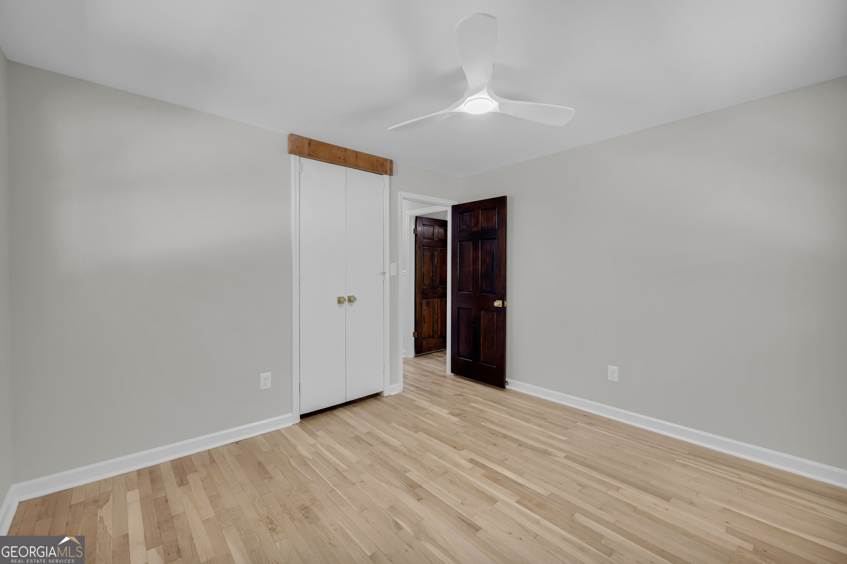 Empty room with hardwood floors, ceiling fan, double-door closet, and dark wood doors.