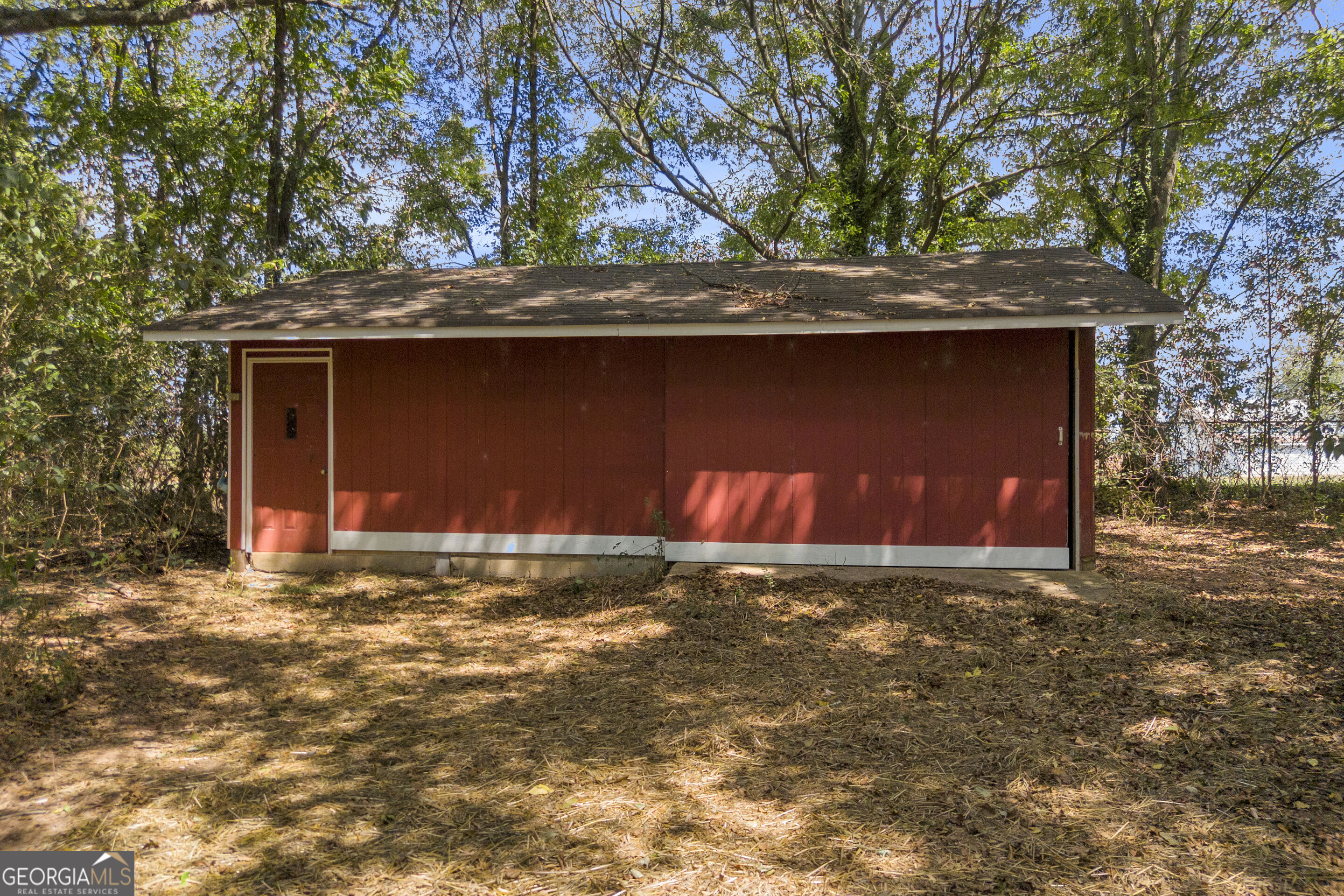 Red outbuilding with white trim and a single door in a wooded clearing.