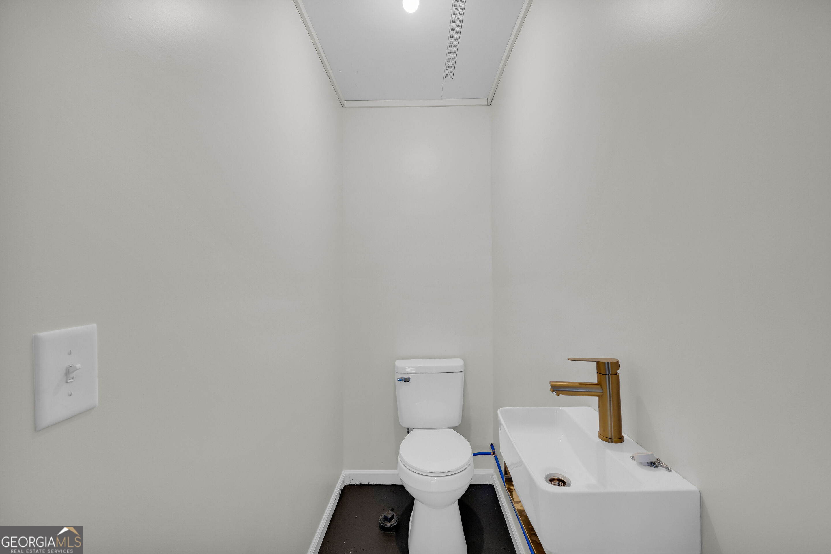 Small bathroom with a white toilet and sink, brass-colored faucet, and exposed blue plumbing.