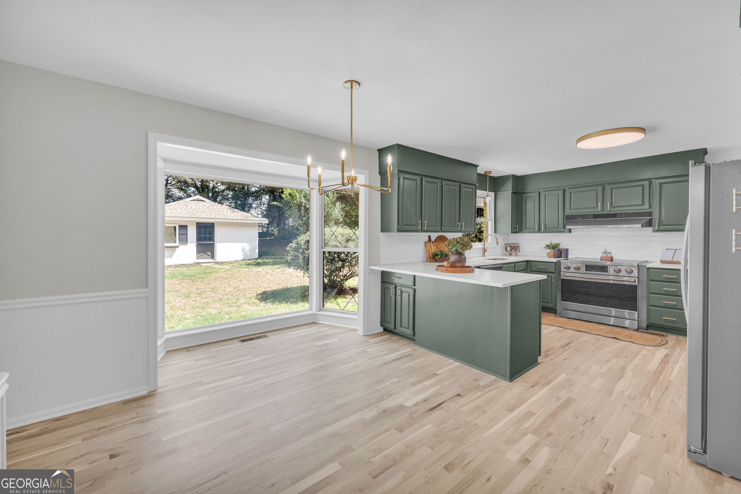 Kitchen with sage-green cabinets, a white island, stainless appliances, and a large corner window.