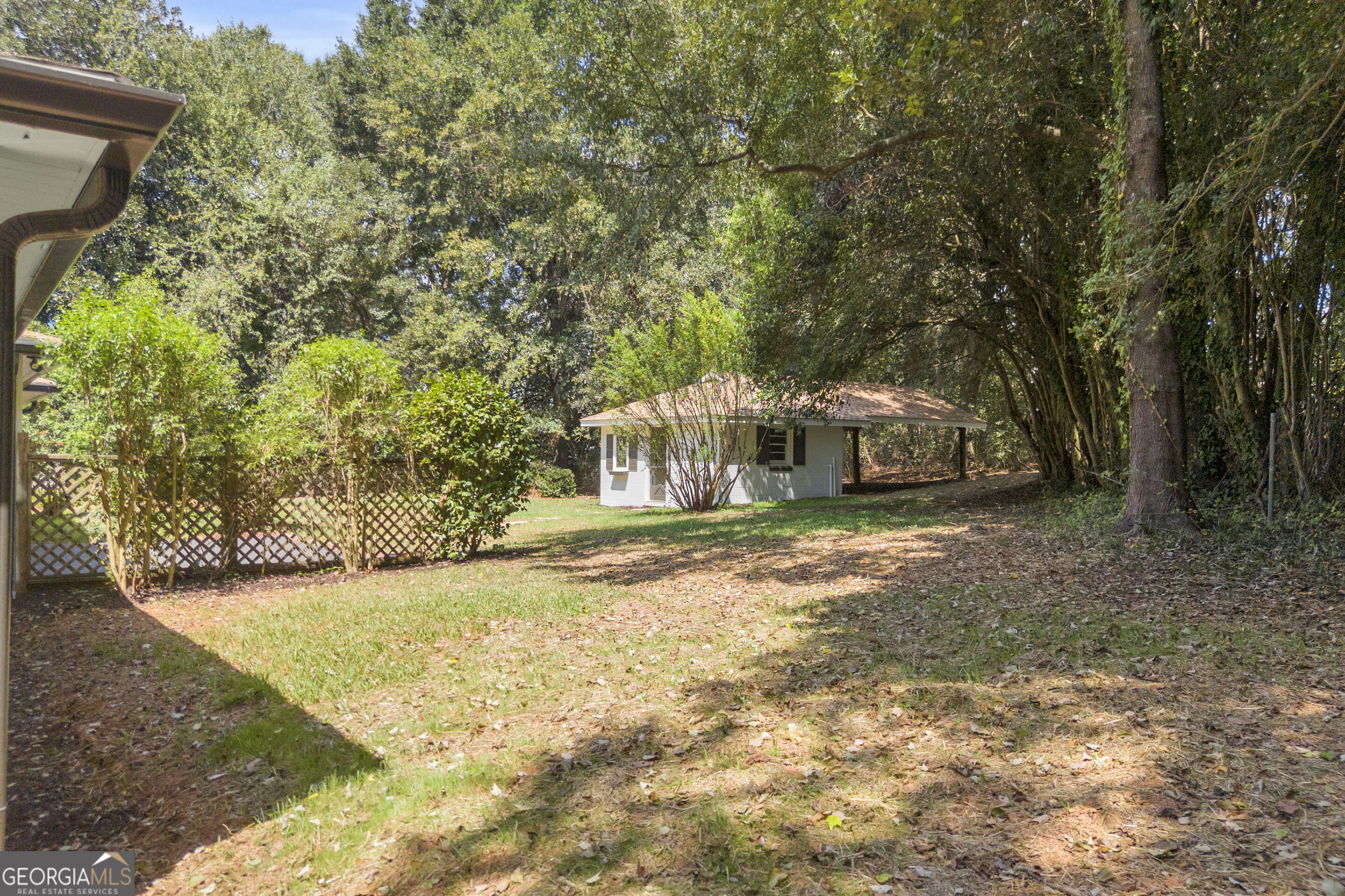 Wooded backyard with a small detached outbuilding and covered carport.