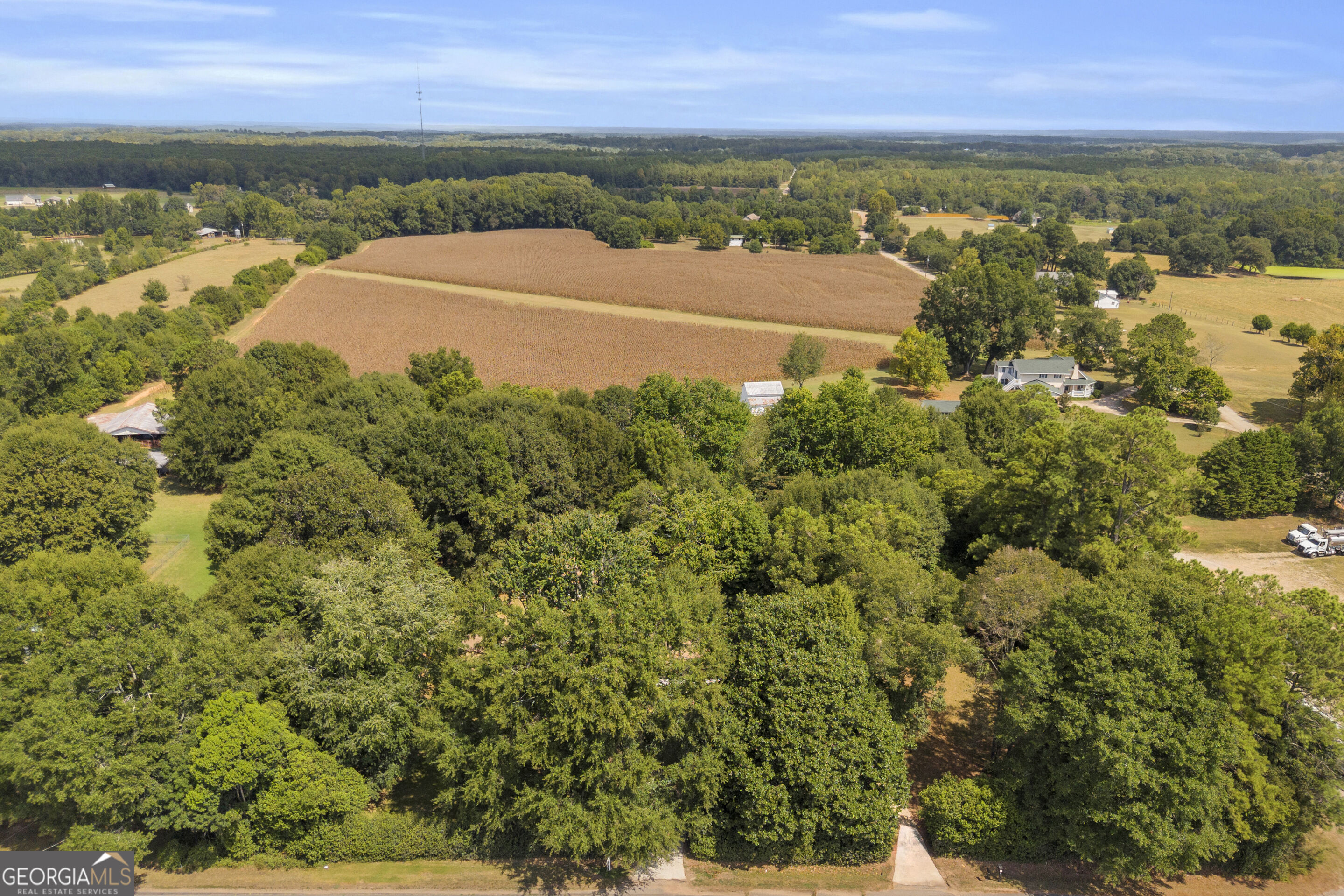 Aerial view of a rural property with a broad cultivated field bordered by dense woods and scattered homes.