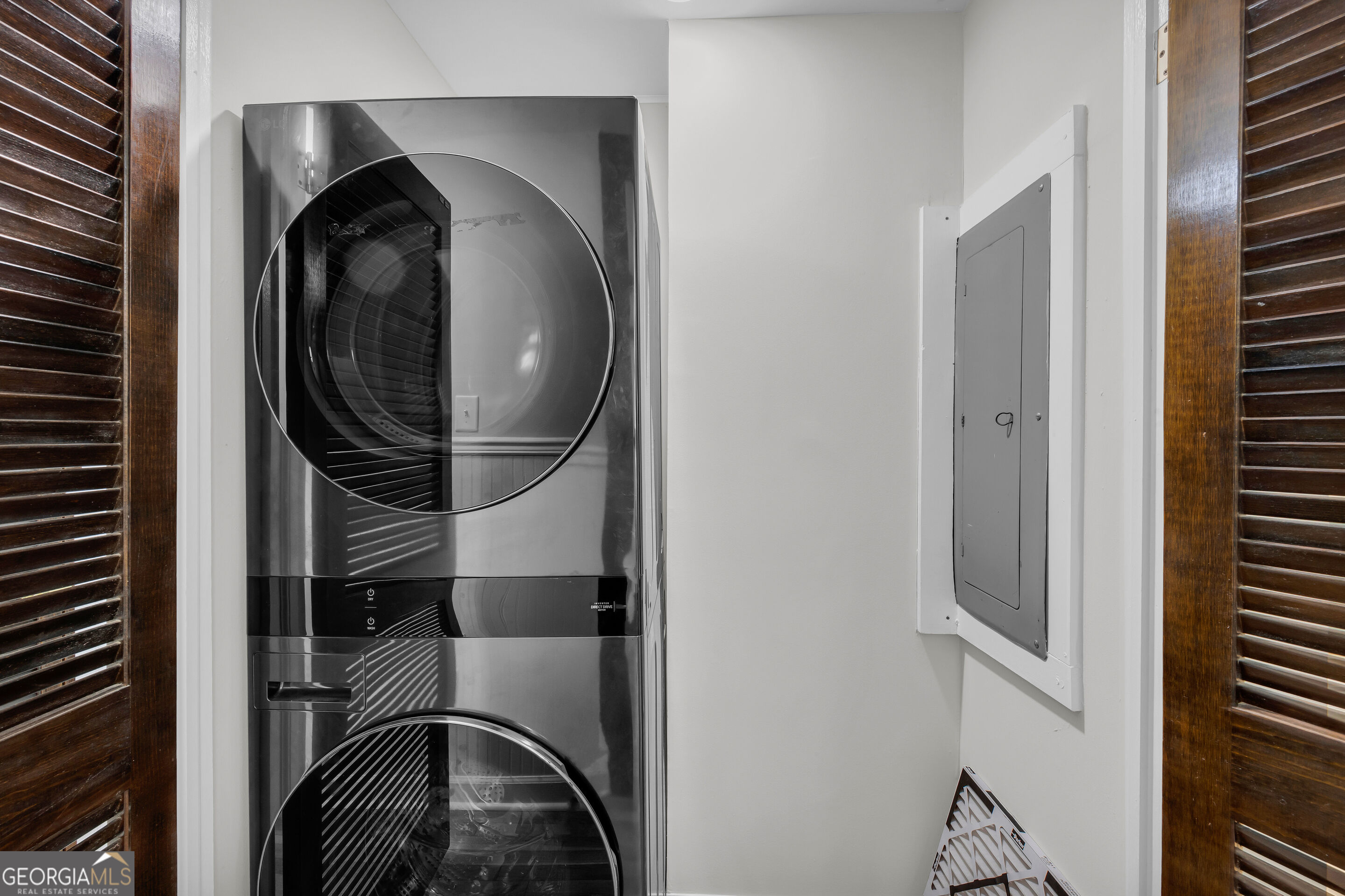Stacked washer and dryer in a laundry closet beside an electrical panel.