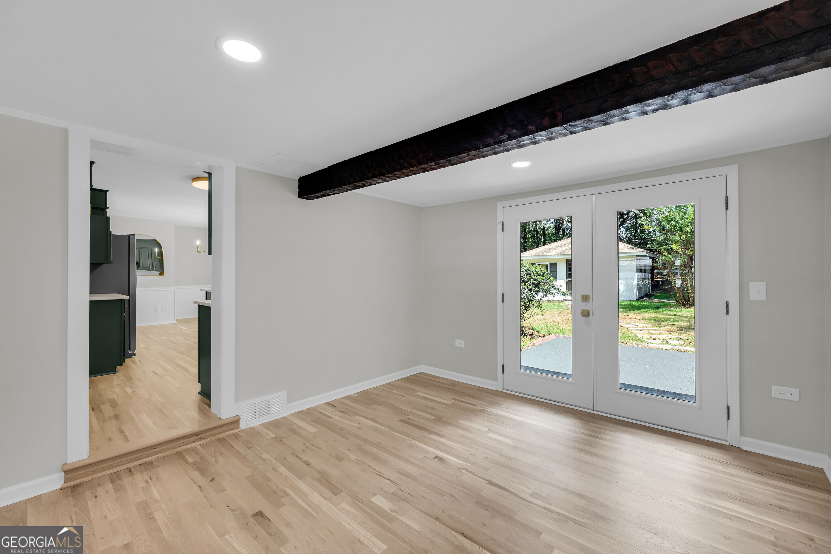 Vacant room with light wood floors, a dark ceiling beam, and double glass doors to the yard.