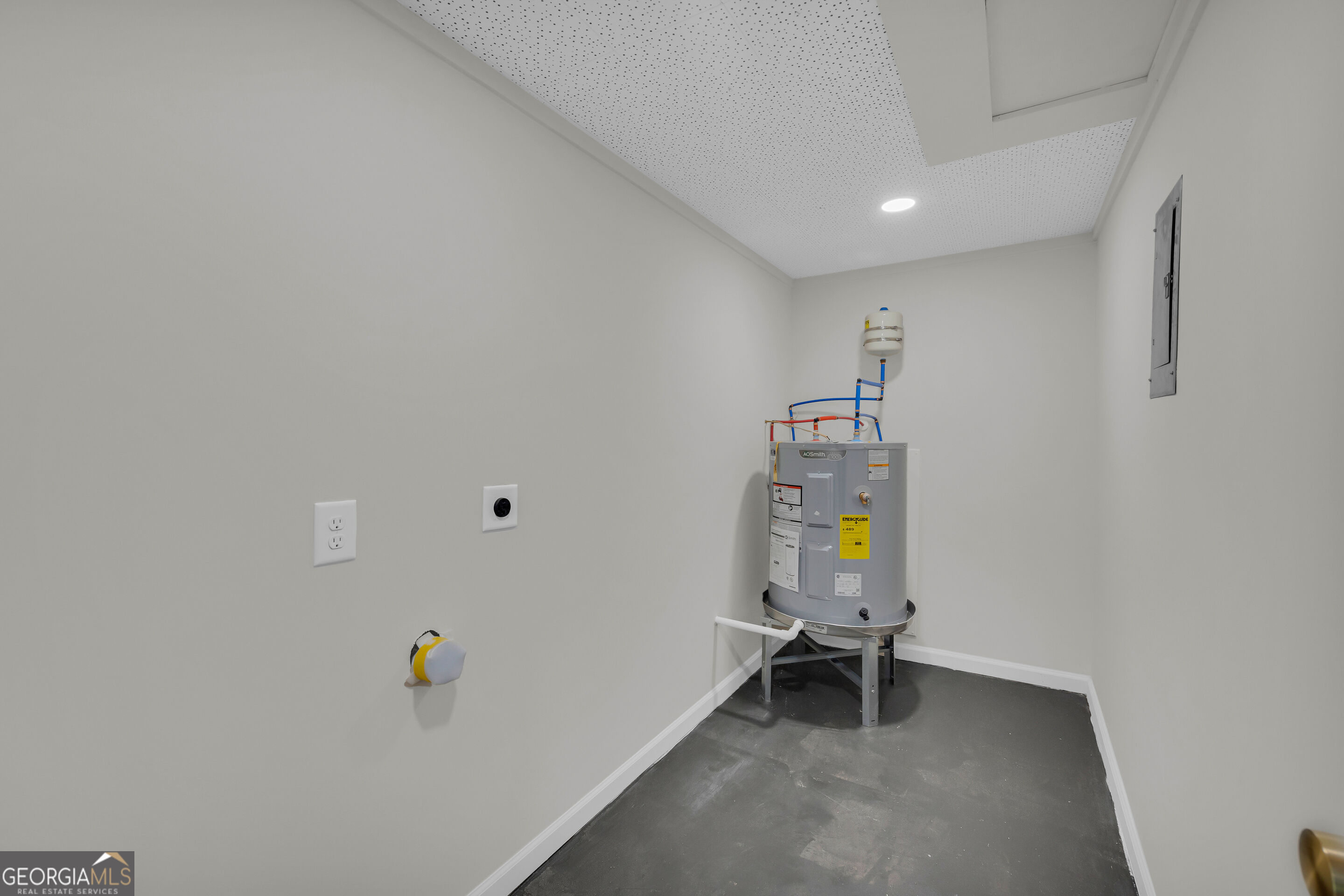 Empty utility room with a gray water heater, exposed plumbing, and concrete floor.