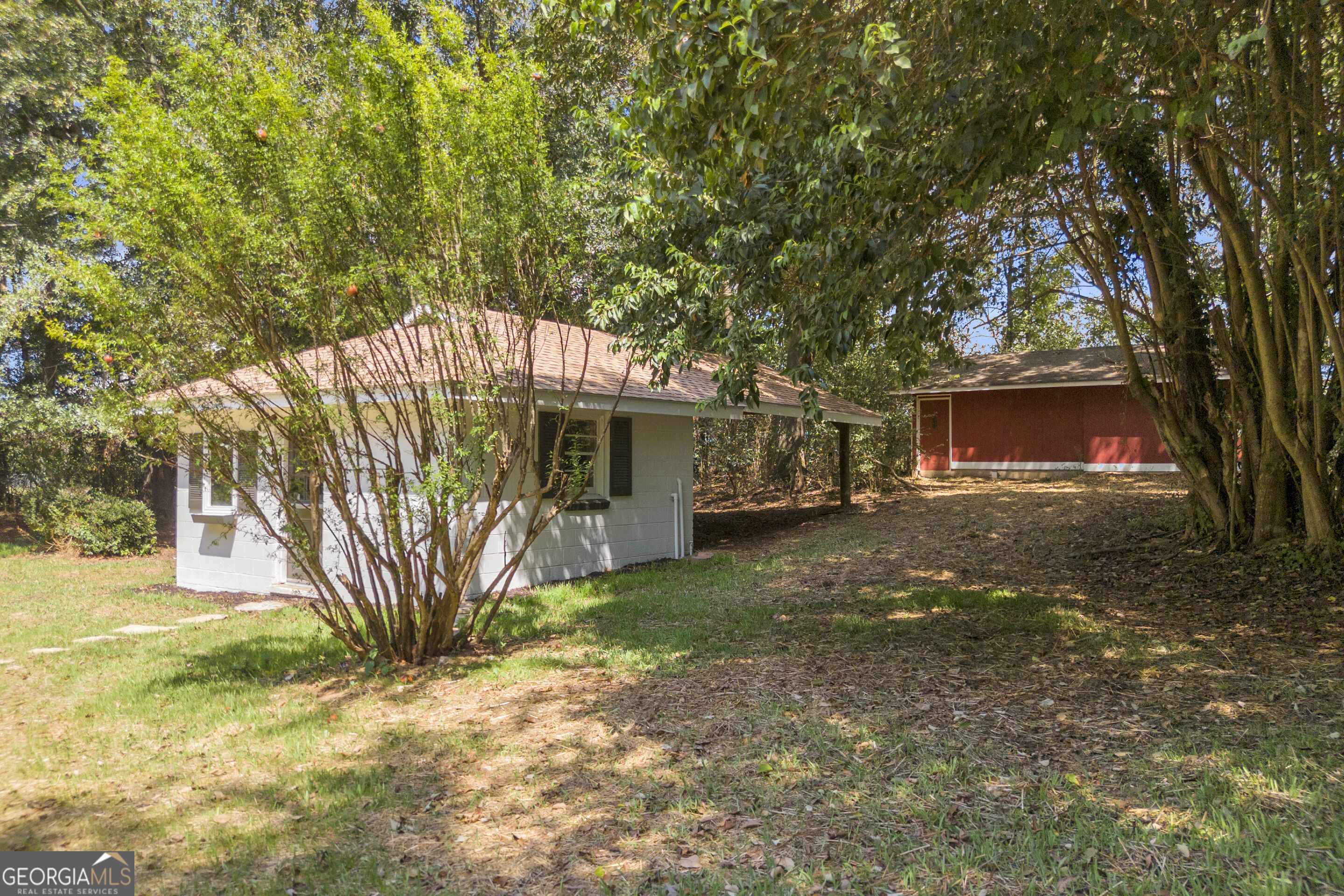 Small house and red outbuilding nestled among mature trees in a shaded yard.